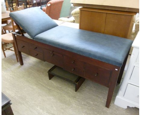 A mid 20thC stained pine patients bench with a blue faux hide adjustable top, over an arrangement of drawers and doors, raise
