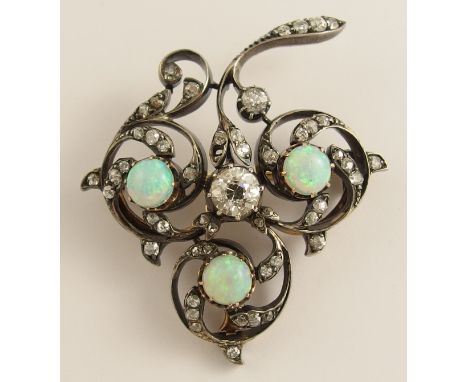 An opal and diamond brooch of scrolling foliate forms in white metal topped yellow metal set through out with diamonds in cut