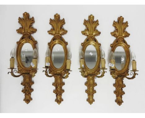 A set of four two light girandole wall lights, the oval mirrored backs, with scrolling crests, each 72cm tall (4)