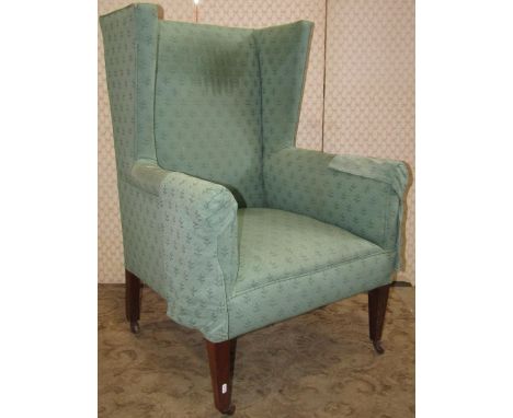 An Edwardian wing armchair with green ground repeating floral sprig patterned upholstery raised on simple square tapered fore