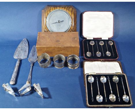 A cased set of six silver coffee spoons another set of silver plated coffee spoons, napkin rings, cake knives, an oak baromet