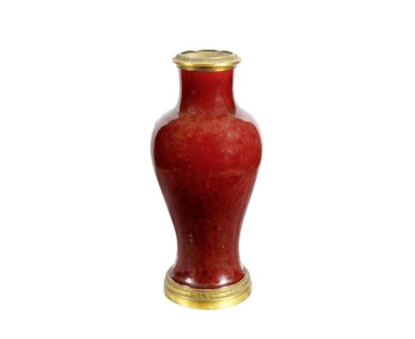 AN ANTIQUE CHINESE PORCELAIN VASE of inverted baluster form and glazed in ox blood red with ormolu mounts to the top and bott