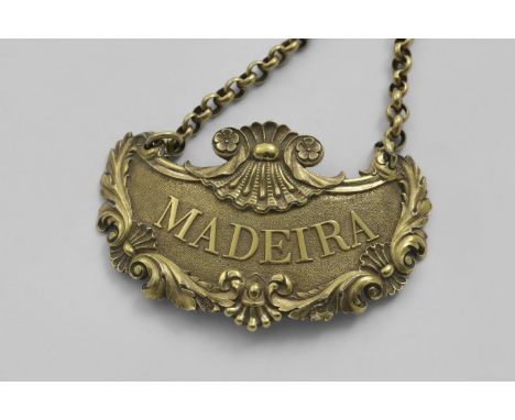 BY PAUL STORR:- A George III cast silvergilt wine label, escutcheon-shaped with textured finish and a border of foliate scrol