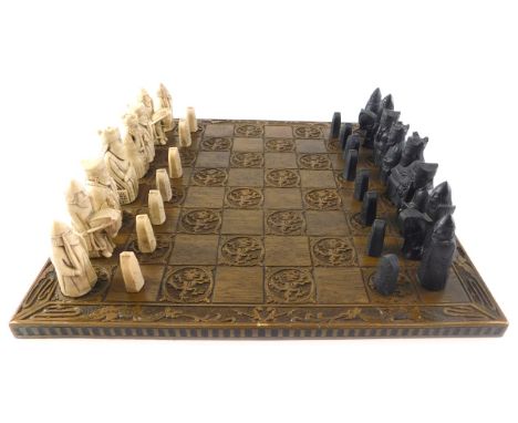 A chess set, with medieval style resin pieces, the oak board carved with heraldic dragons, etc., 45cm wide. 