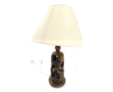 An African carved hardwood tribal table lamp base, decorated with figures, etc., and a cream shade, 62cm high overall. 