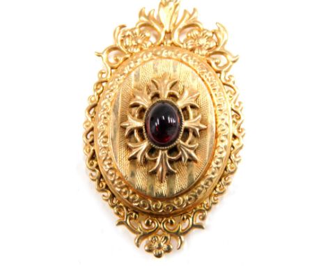 An Edwardian 9ct gold pendant and chain, the oval locket set with cabochon ruby, with scroll and engine turned decoration, in