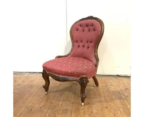 A Victorian walnut nursing chair, c. 1860, the shaped button-upholstered back with carved crest and corresponding seat rail, 