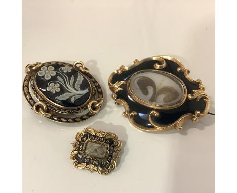 A group of three 19th century yellow metal and enamel mourning brooches: the first of shaped oval form, centred by a glazed h