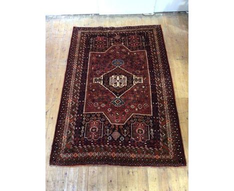 A Shiraz hand-knotted wool small carpet, the madder field with indigo framed medallion and corresponding spandrels within mul