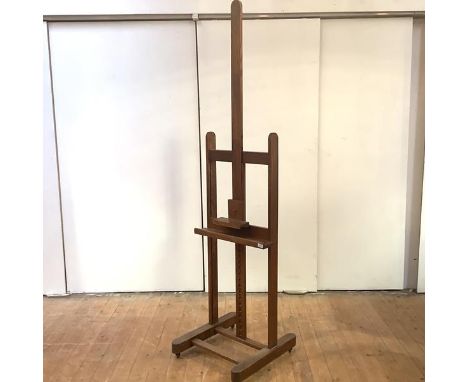 An elm easel, first half of the 20th century, the adjustable trestle frame, raised on castors. 264cm (fully extended) by 59cm