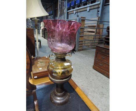 A Victorian style oil lamp, having wooden base base, amber glass reservoir and cranberry shade