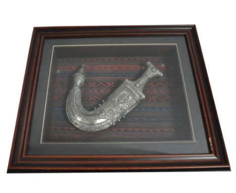 Saudi Bedouin khanjar, the shaped blade on hilt and under scabbard mounted by white metal, mounted and framed, 49 x 43cms.