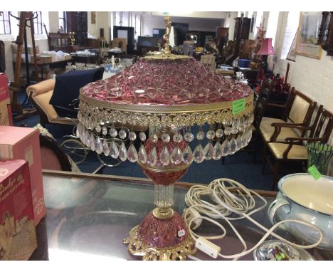 A cranberry glass table lamp on a brass frame with clear glass droplets