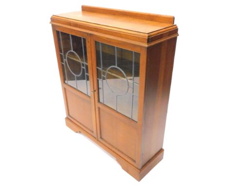 A mid 20thC oak display cabinet, the top with a raised back above two doors each with leaded glazed panels, above two unglaze