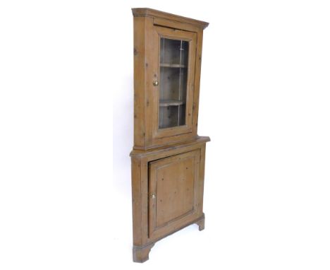 A pine standing corner cabinet, the top with a moulded cornice, single glazed door, the base with a panelled door on bracket 