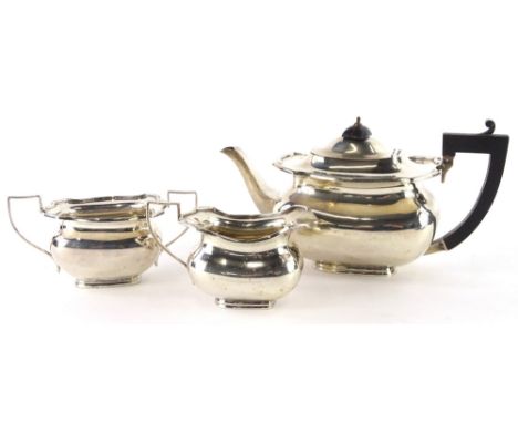 A George V silver three piece tea set, of rectangular form with moulded shaped borders, comprising teapot with ebonised knop 