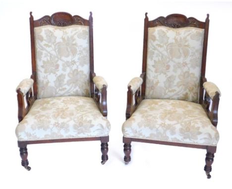 A pair of late 19th/early 20thC walnut armchairs, each with a padded back, arm rests and seat, on turned tapering legs, with 