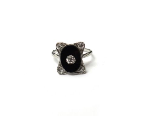 A platinum, diamond and black onyx ring, in a curved rectangular panel shaped Art Deco design, centred by a collet set cushio
