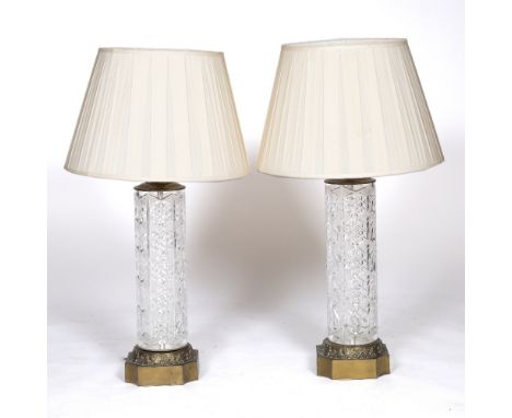 A PAIR OF CUT GLASS AND BRASS MOUNTED TABLE LAMPS of cylindrical form with hobnail cut decoration and shaped leaf moulded cas