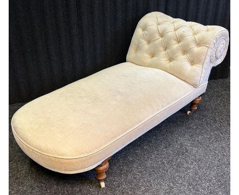 A Victorian chaise long, raised on turned legs ending in ceramic casters, the whole covered in a neutral upholstery with a bu