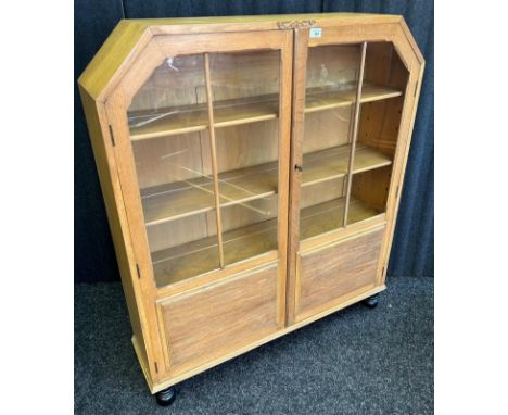 An art deco light oak, display cabinet the glazed doors opening to three shelves, raised on turned legs. With key [ 123 x 107