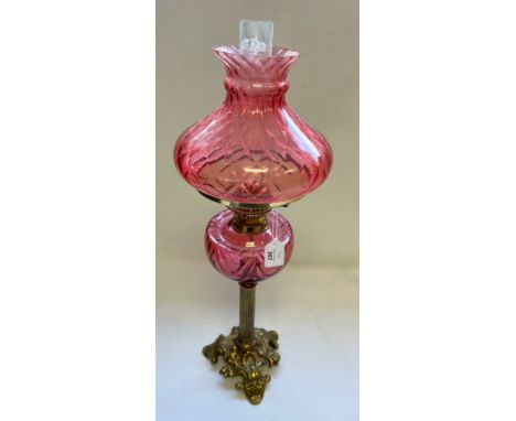 Antique brass oil lamp with Cranberry flutted shade and reservoir on a fluted column and quadripartite foliate base.