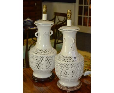 A pair of Chinese blanc de chine lamp bases, decorated with figures within a pierced background, raised on circular wood stan