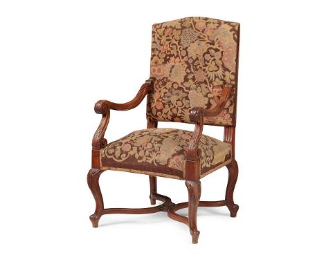 FRENCH WALNUT ARMCHAIR 19TH CENTURY the arched padded back above a wide stuff-over seat flanked by leaf carved scrolling open