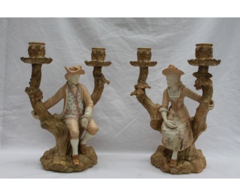 A pair of Royal Worcester Watteau style figural candelabra, each modelled as young male and female subjects seated on twin br