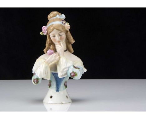 A Goebel half-doll,  with blonde painted hair with bun and falling ringlets, flowers and blue ribbon in hair, holding a rose 