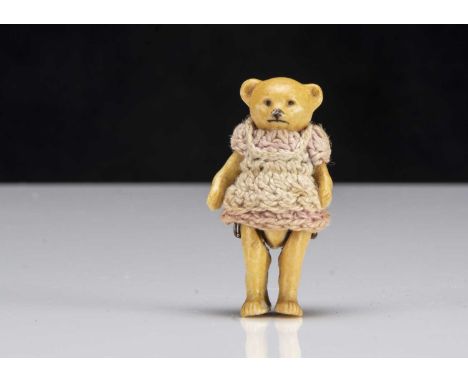 A Hertwig all-bisque teddy bear dolls’ house doll, painted with pin jointed arms and legs, crochet dress —1 3/4in. (4.5cm.) h