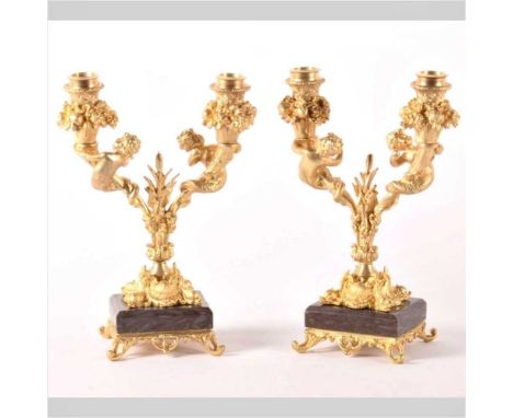 A pair of gilt bronze twin branch table candelabra, each decorated with putti and mounted upon a polished hardstone plinth, h