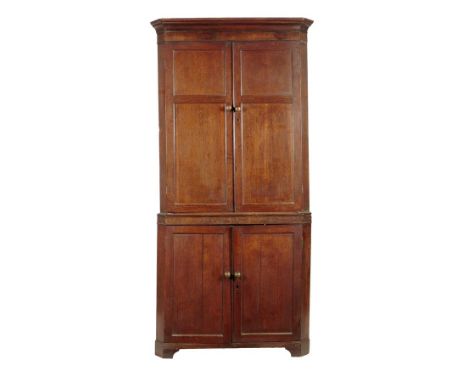 A late George III oak standing corner cupboard, with two pairs of panelled cupboard doors, the top section with three shaped 