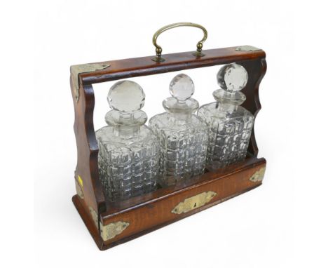 An early 20th century three bottle oak tantalus, with silver plated mounts and containing three cut glass decanters  35 by 14