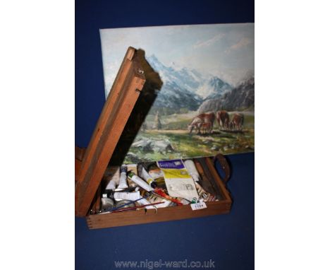 An artist's Easel with paints and brushes together with oil painting of rural scene.