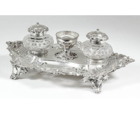 An early Victorian silver oval inkstand of shaped and moulded outline, with scroll mounts and pierced rims, on scroll panel f