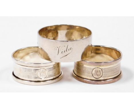 Three George V silver napkin rings, to include a pair of engine turned decorated napkin rings, with a central circular shield