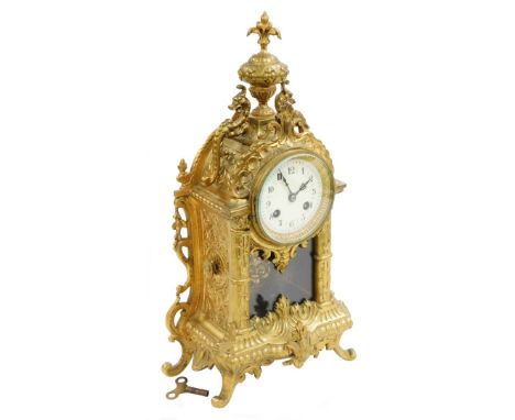 A French cast brass mantel clock, the domed top with a fleur de lis finial and applied with two dragon, with a cream enamel c