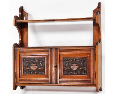 A late Victorian walnut wall shelf, with two fielded panelled doors, carved with urns and scrolls, 60cm high, 62cm wide, 14cm