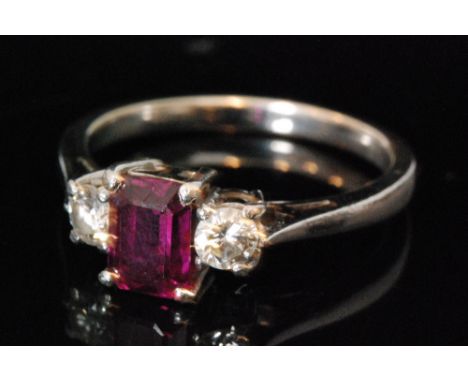 A ruby and diamond three stone ring, two brilliant cut diamonds beside central emerald cut ruby, to plain white metal chenier