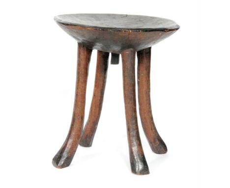 An African tribal hardwood stool, possibly East African, with a dished circular seat above four splayed legs, height 36cm and