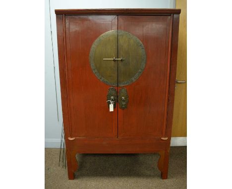 An early 20th Century Chinese red lacquer wardrobe, the caddy top above a pair of cupboard doors, with inset brass plaque and
