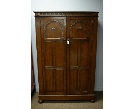 An early 20th Century oak two-door wardrobe, the projecting cornice above a lunette carved frieze, with two arcaded panel doo