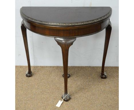 An early 20th Century mahogany demi lune card table, the shaped top with acanthus moulded edge, enclosing a baize-lined inter