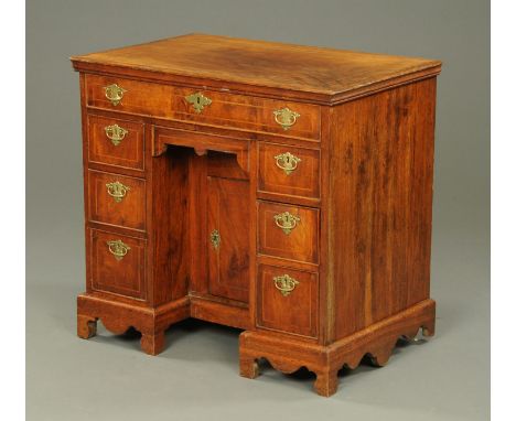 A Georgian walnut veneered kneehole desk, fitted with a series of drawers and recessed cupboard and raised on bracket feet.  