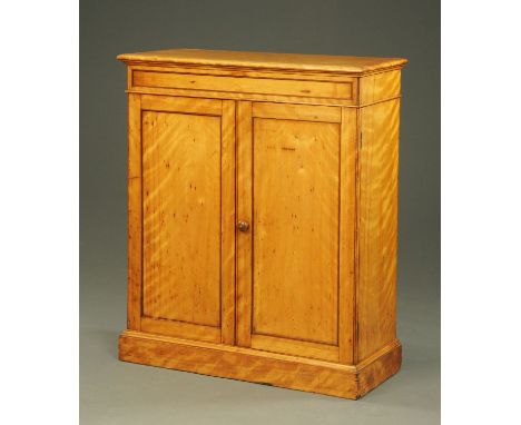 A satin birch cupboard in the manner of Holland, with moulded cornice above a pair of panelled cupboard doors with wooden kno