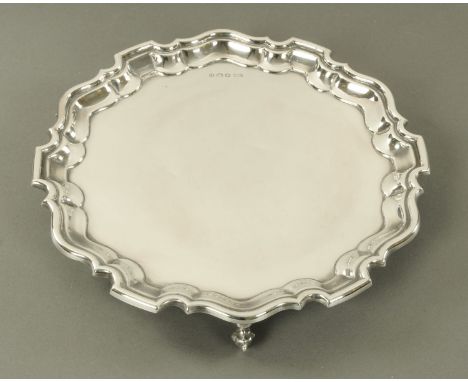 A silver salver, Viners, Sheffield 1937, with shaped and raised border supported upon three scroll capped feet.  Diameter 25.