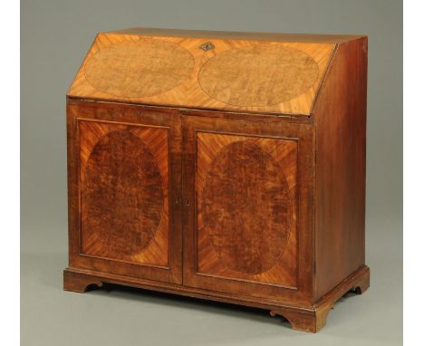 A George III mahogany estate bureau, the flap with oval panels and with cupboard base opening to two slides and six drawers a