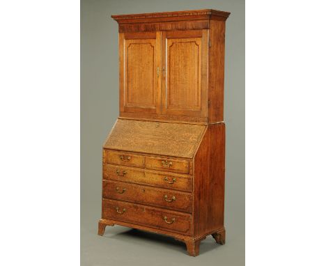 An early 19th century oak bureau bookcase, with moulded cornice above a pair of panelled cupboard doors, the base with crossb