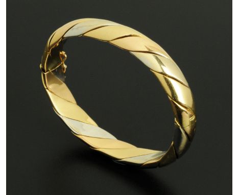 An 18 ct tricolour gold hinged bangle, makers mark "CG" and hallmarked for London 1988.  Interior diameter 6 cm, 49.2 grams (